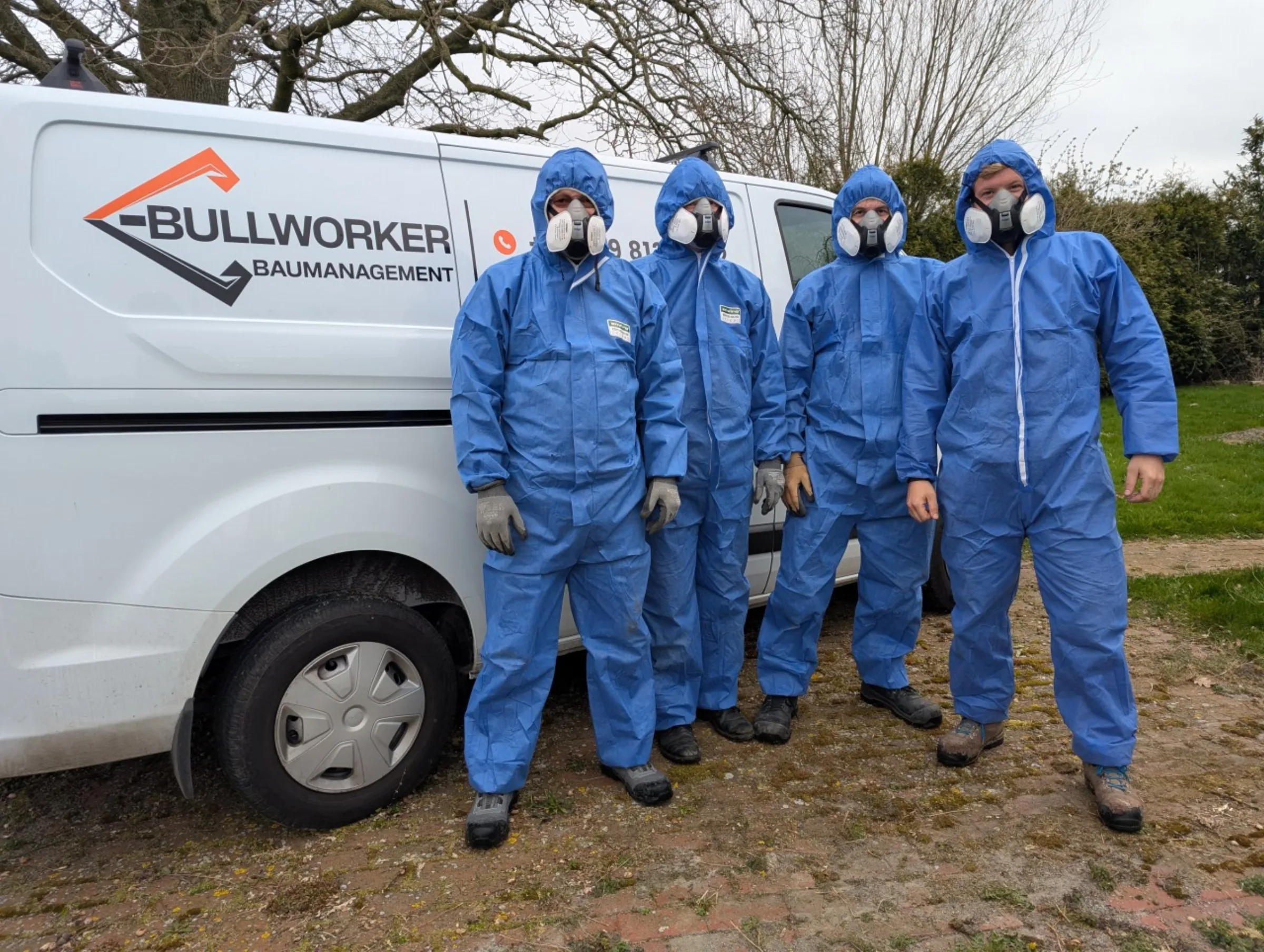 Team von Bullworker-Tiefbau in blauen Schutzanzuegen mit Atemschutz vor dem Firmen-Transporter